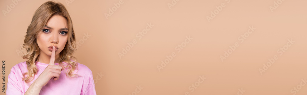 serious young woman looking at camera and showing hush gesture isolated on beige, banner. serious young woman looking at camera and showing hush gesture isolated on beige, banner.