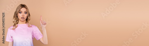 Wallpaper Mural thrilled woman looking at camera and pointing up with finger isolated on beige, banner. Torontodigital.ca