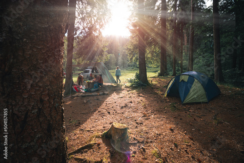 Peoples meets the evening, sunset in the forest. Tourist tent. Camping an reacreation. Beautiful pine forest in mountains. Sunbeams. photo