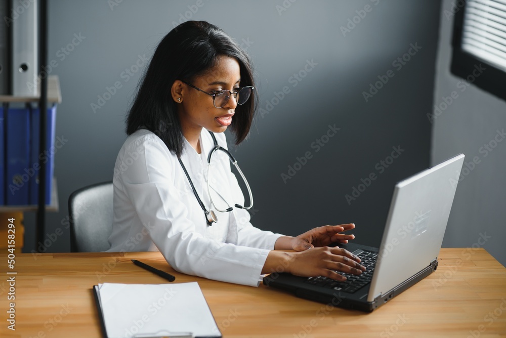 Portrait of young indian doctor working in the hospital while looking at laptop and write on clipboard. Portrait of young indian doctor working in the hospital while looking at laptop and write on clipboard.