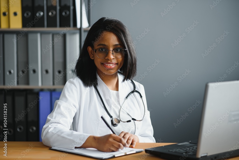 Smiling young adult indian female doctor wear white coat in medical clinic office. Happy beautiful health care india professional medic physician, therapist, headshot portrait Smiling young adult indian female doctor wear white coat in medical clinic office. Happy beautiful health care india professional medic physician, therapist, headshot portrait