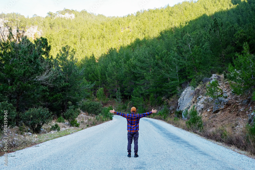 Obraz premium Male traveler wearing flannel shirt enjoying beautiful view of a mountain switchback road. Man experiencing spiritual uplifting from being alone in nature. Scenic background, copy space, back view.