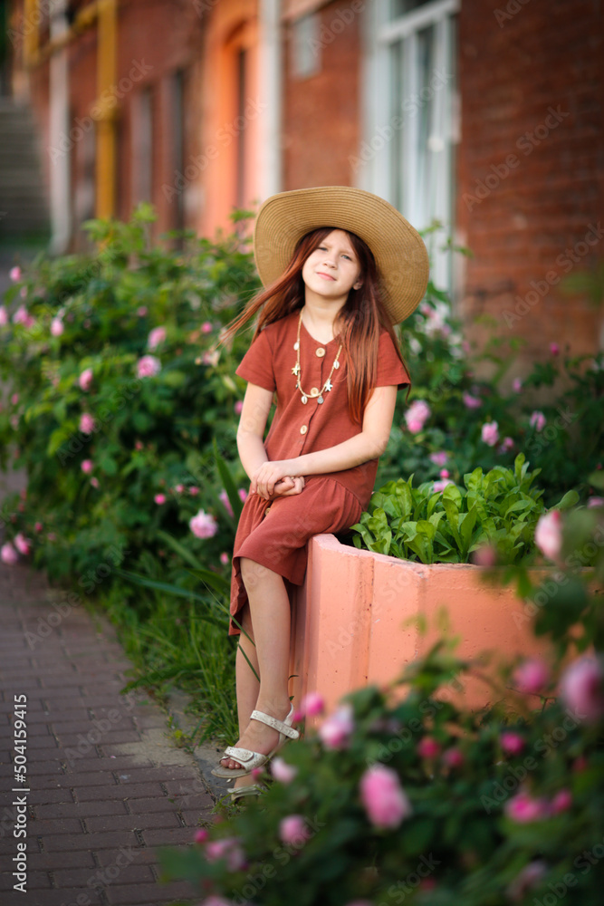 Cute kid girl in hat near blooming flower bed in city