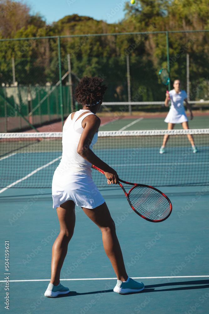 African american female player playing tennis game with caucasian competitor at court on sunny day