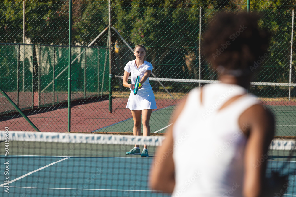 Caucasian female player serving tennis ball to competitor at court on sunny day Caucasian female player serving tennis ball to competitor at court on sunny day