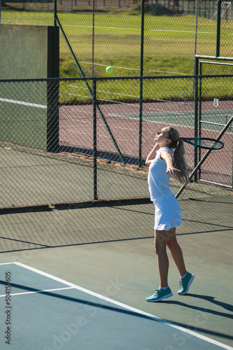 Full length of young female caucasian player serving ball with racket at tennis court on sunny day