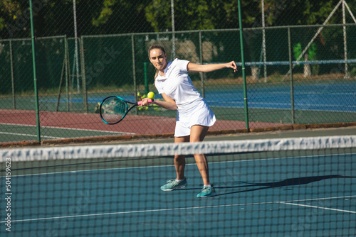 Full length of young female caucasian player hitting ball with racket at tennis court on sunny day