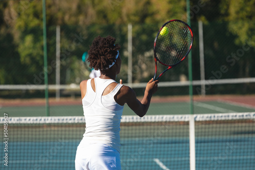 African american female player hitting ball with racket at tennis court on sunny day