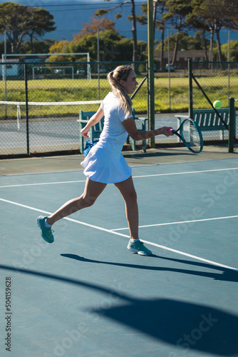 Full length of young female caucasian player hitting ball with racket at tennis court on sunny day © wavebreak3