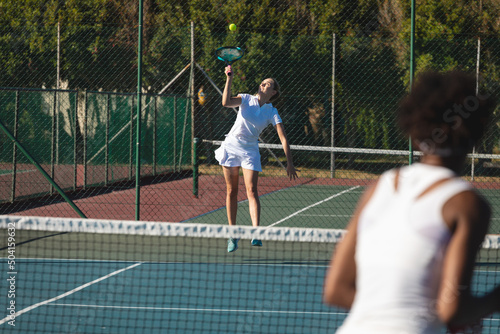 Young female caucasian player serving to african american competitor at tennis court on sunny day