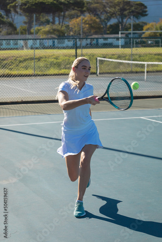 Full length of young female caucasian tennis player hitting ball with racket at court on sunny day
