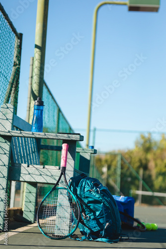 Tennis racket and backpack by empty wooden bench at court on sunny day