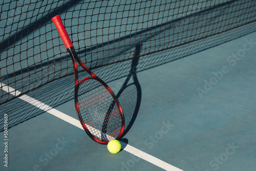 High angle view of red racket with ball leaning on net at tennis court during sunny day