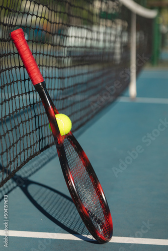 Ball with red racket leaning on tennis net at court during sunny day