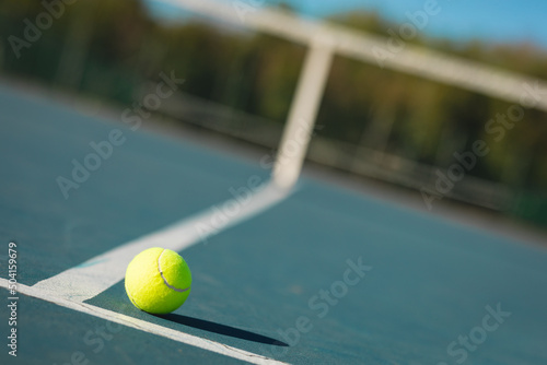 Close-up of green tennis ball by line on empty court during sunny day