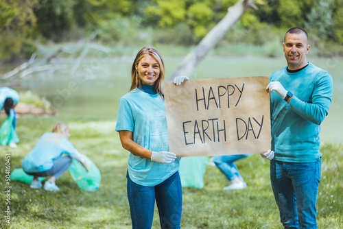 Happy volunteers holding placard with 'happy Earth day' message. Group of people, cleaning together in public park, saving the environment together. Happy Earth day!