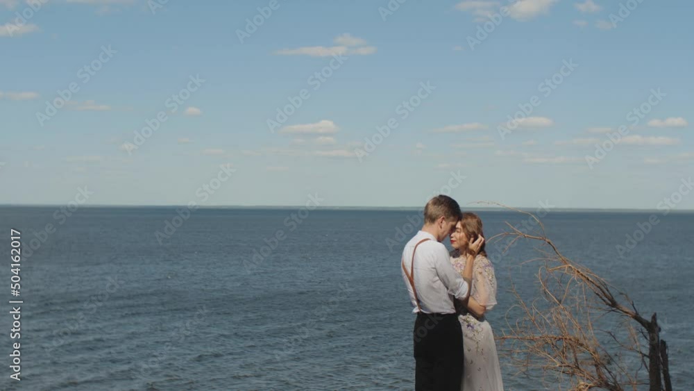 Couple in love hugs, the couple stands opposite each other with their eyes closed, the sea is in the background, the wind develops female hair. Couple in love hugs, the couple stands opposite each other with their eyes closed, the sea is in the background, the wind develops female hair.