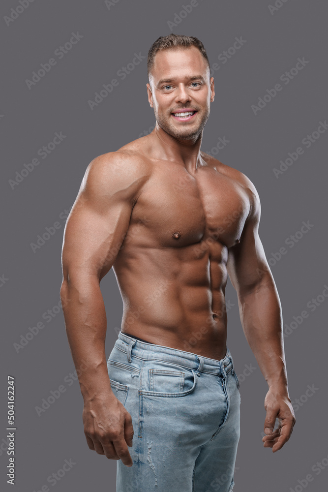 Fototapeta premium Studio shot of handsome guy with muscular build dressed in jeans posing against grey background.