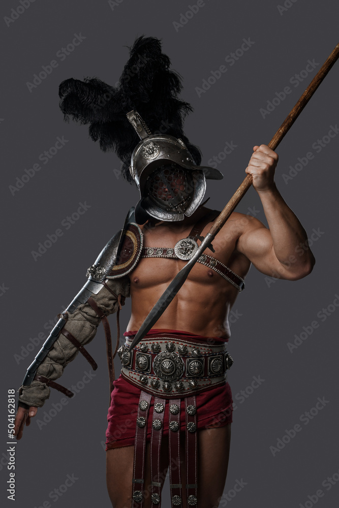 Shot of ancient roman fighter with plumed helmet throwing spear against grey background. Shot of ancient roman fighter with plumed helmet throwing spear against grey background.