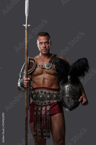 Studio shot of antique gladiator holding helmet plumed with black feathers and long spear.