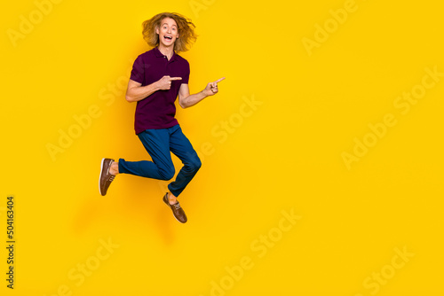 Fototapeta Naklejka Na Ścianę i Meble -  Full size photo of overjoyed energetic man jumping direct fingers empty space isolated on yellow color background