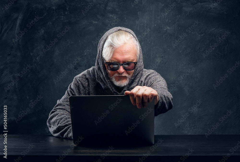 Studio shot of grandfather dressed in sunglasses and grey hoody using modern laptop. Studio shot of grandfather dressed in sunglasses and grey hoody using modern laptop.
