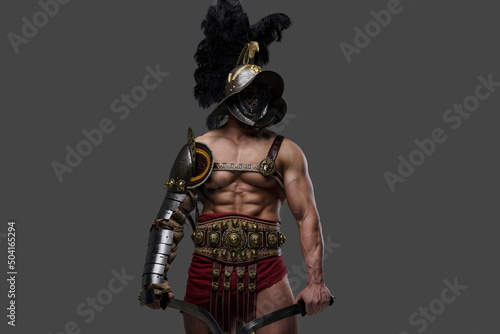 Studio shot of antique gladiator with muscular build and two swords isolated on gray background.
