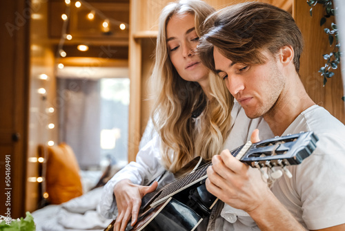 Man playing guitar, singing song on small kitchen,cooking in van. Young girl,guy just married couple,lovers traveling in camper,house on wheels,trailer,motor home. Love romantic road travel vacation