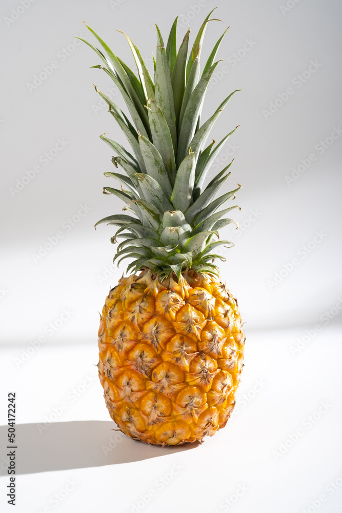 Juicy pineapple on a white background. A whole pineapple and a cut off half. Palm tree shade, creative lighting. Juicy pineapple on a white background. A whole pineapple and a cut off half. Palm tree shade, creative lighting.