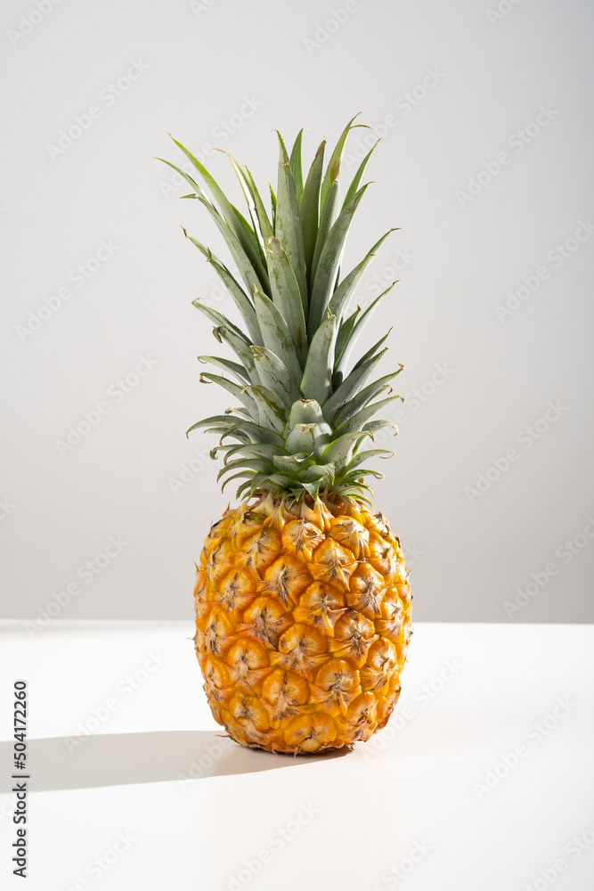 Juicy pineapple on a white background. A whole pineapple and a cut off half. Palm tree shade, creative lighting. Juicy pineapple on a white background. A whole pineapple and a cut off half. Palm tree shade, creative lighting.