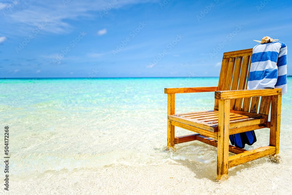 A wooden chair standing in the Indian Ocean with a towel, shell and flippers.