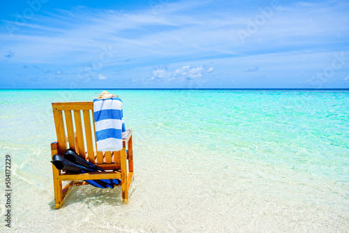 A wooden chair standing in the Indian Ocean with a towel  shell and flippers.
