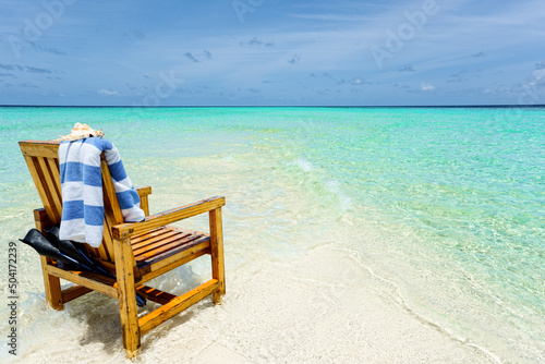 A wooden chair standing in the Indian Ocean with a towel, shell and flippers. © BRIAN_KINNEY