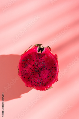 Juicy ripe pitahaya whole and scattered on a pink background. View from above. Hard light, shadow from a palm tree. Thai tropical fruits.
