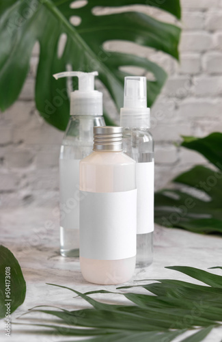 Trasparent cosmetic dispensers and monstera leaves on marble table close up. Brand packaging mockup