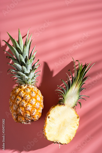 Juicy pineapple on a pink background. A whole pineapple and a cut off half. Palm tree shade, creative lighting. Exotic fruits and vitamins.
