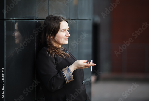 Elegant woman with cigarette in an urban setting. Businesswoman posing sideways in the street. Selective focus.