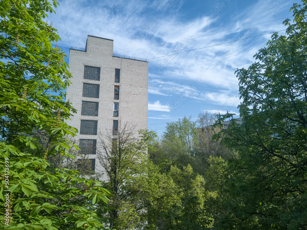 An old soviet residential building in green trees with beautiful blue sky behind. Close-up.