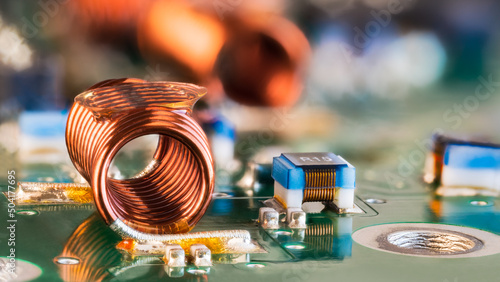 Orange wire winding of air-core coil and PCB electronic components in blurry background. Closeup of radio frequency inductor, small capacitors and resistors on circuit board. Surface mount technology.