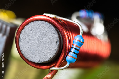 Cylindrical inductor with black ferromagnetic core wrapped by red wire on PCB detail. Closeup of small blue carbon resistors with electronic color code soldered on coil winding with blurry background. photo