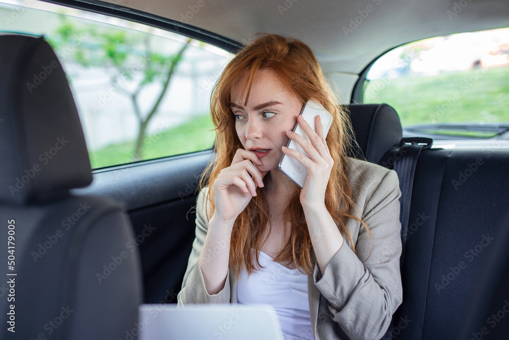 Businesswoman talking on the mobile phone and using the laptop in the car Businesswoman talking on the mobile phone and using the laptop in the car