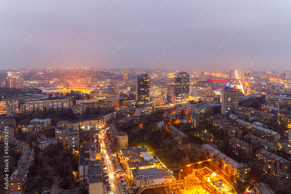 Obraz premium Ukraine, Kyiv – March 12, 2016: Aerial panoramic view on central part of Kyiv city from a roof of a high-rise building. Night life in a big city. Foggy and rainy weather. 