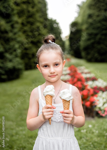 Little girl eats ice cream in the park. The child enjoys ice cream in the summer. The girl is holding an ice cream cone in her hands.