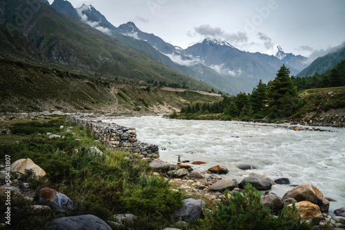 View of Baspa river flanked by boulders and Himalayas under overcast sky. Chitkul, India. 
