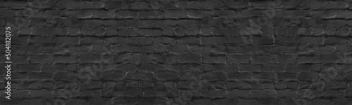 Old black painted plastered brick wall wide texture. Dark gray rough masonry long backdrop. Gloomy grunge panoramic background