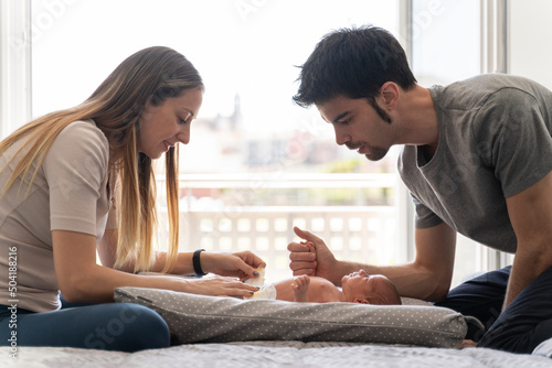 Slika na platnu a couple of parents changing the diapers to their newborn son on the bed