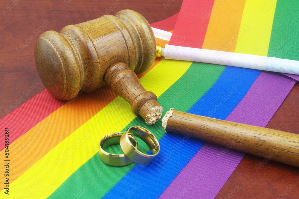LGBT marriage equality and laws concept. Two wedding rings, broken wooden gavel and LGBT flags 	
