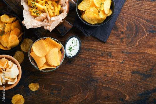 Potato corrugatedchips. Fast food. Crispy potato chips ceramic black bowl with sour cream sauce and onions in wooden stand on old wooden dark background. American tradition. Hot BBQ. Top view