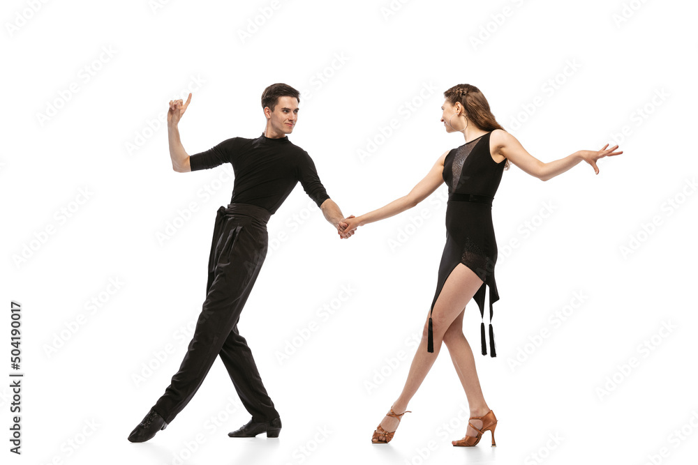 Dynamic portrait of young emotive dancers in black outfits dancing ballroom dance isolated on white background. Concept of art, beauty, music, style. Dynamic portrait of young emotive dancers in black outfits dancing ballroom dance isolated on white background. Concept of art, beauty, music, style.