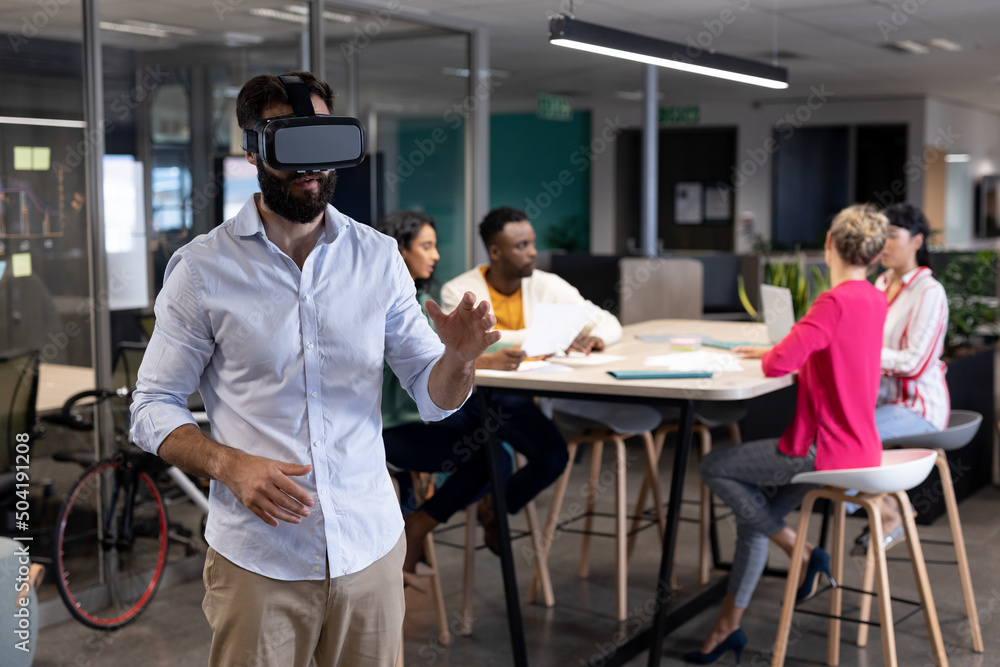 Caucasian businessman wearing vr headset against multiracial colleagues in meeting at workplace